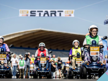 Tom Coronel geeft tips aan Peter die meedoet aan het NK Scootmobiel op Circuit Zandvoort